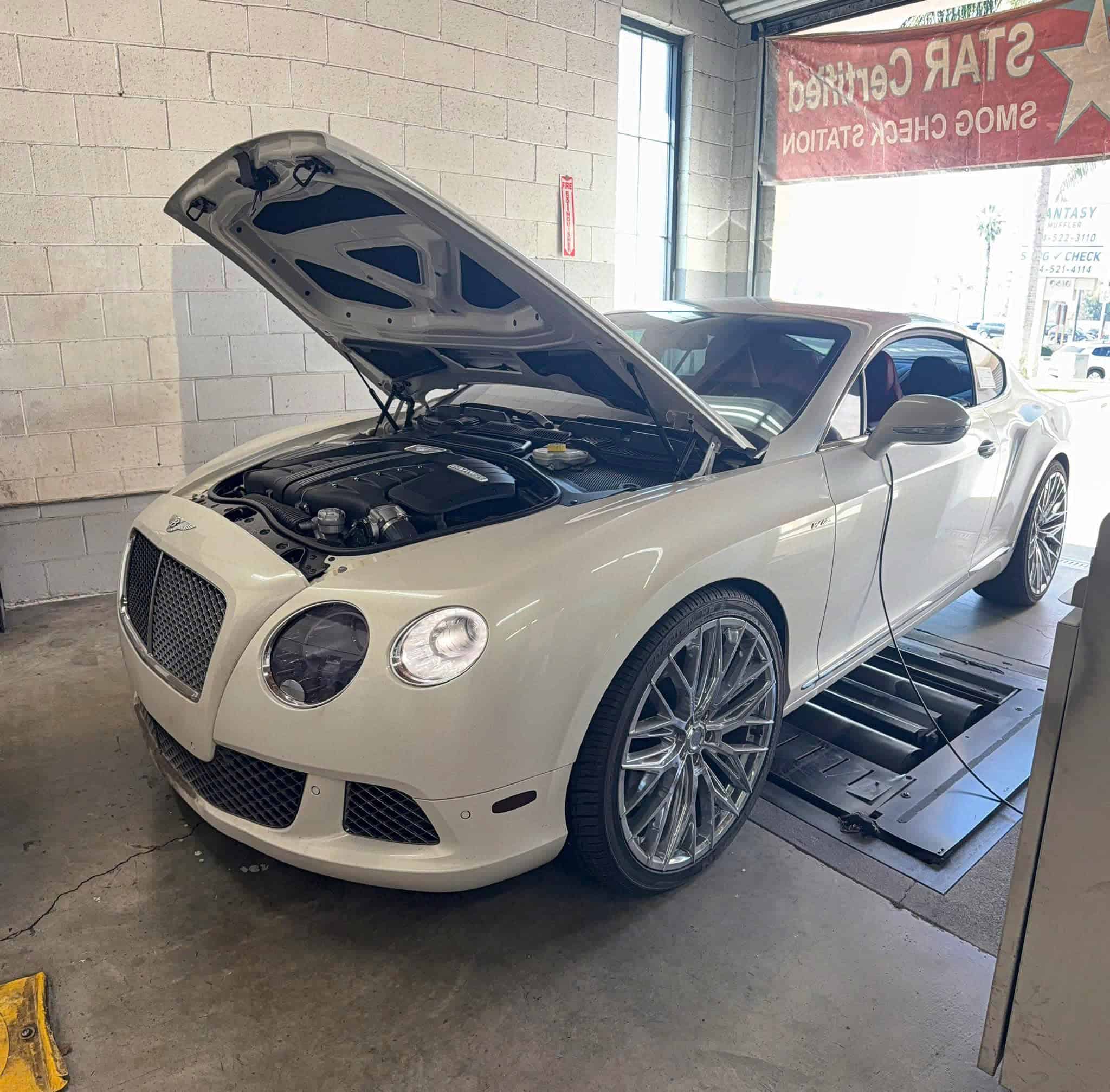 Modern white sports car undergoing smog check at Vu & Vu Smog Check Center.